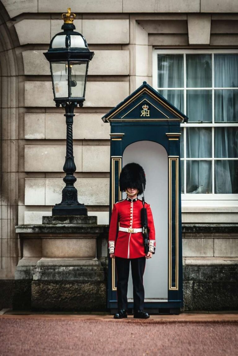 a guard in a red uniform standing in front of Buckingham Palace in London