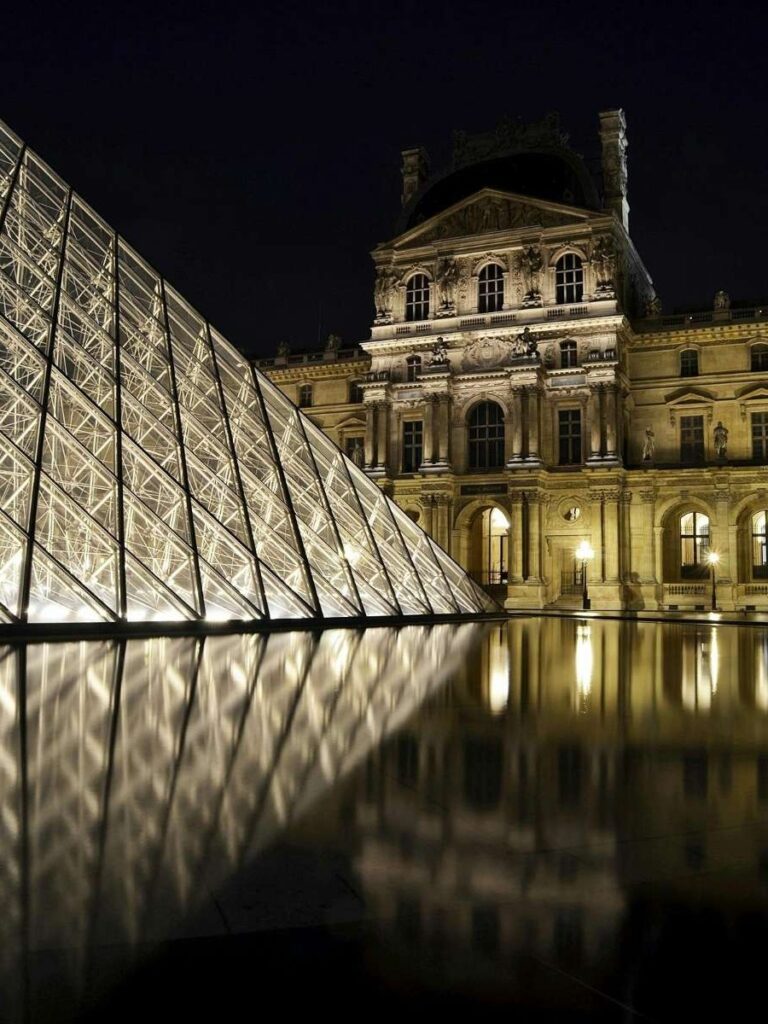 Louvre Museum pyramid and building lit up at nigh