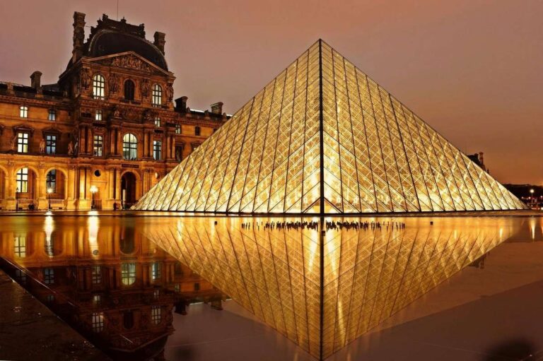 The Louvre Pyramid illuminated at night, reflecting in a pool