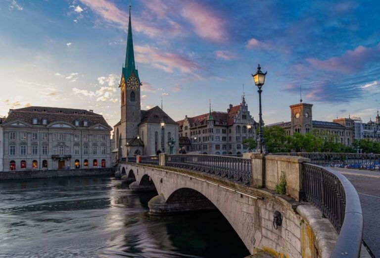 A stone bridge in Zurich with a clock tower against a vibrant sunset