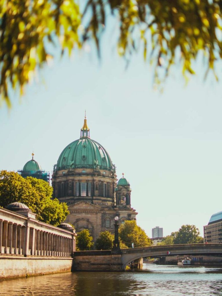 Berlin Cathedral viewed from the river, framed by trees on a sunny day