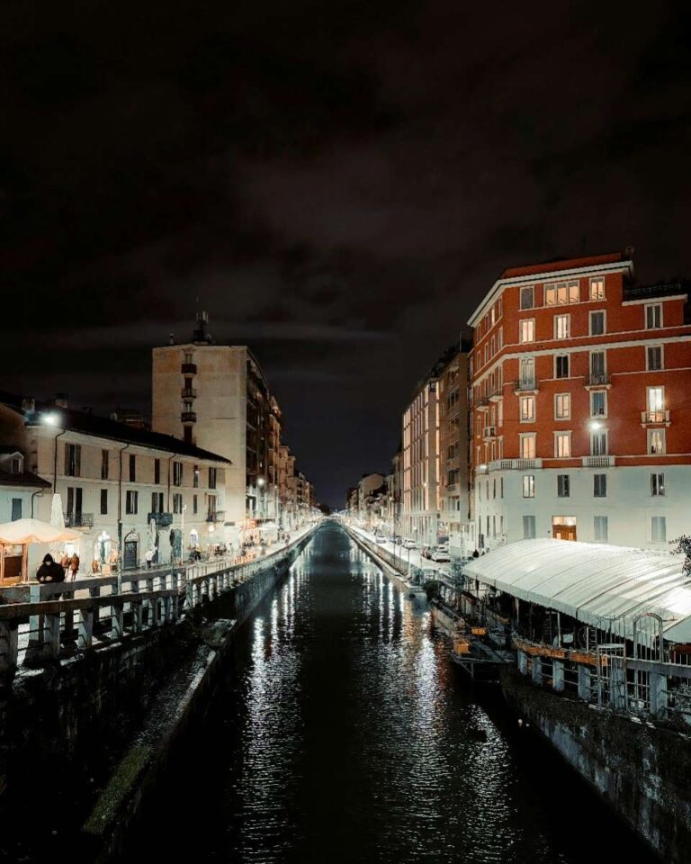 Night view of a river walk in Milan with lit buildings and water