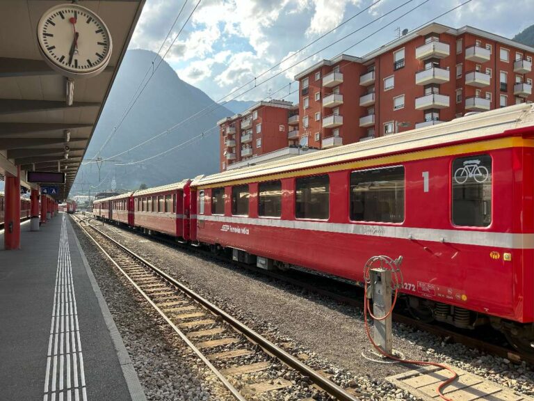 Red Italian regional train at a station with mountains in the background in Tirano