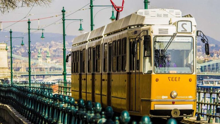 Yellow tram in Budapest traveling alongside the river with city views