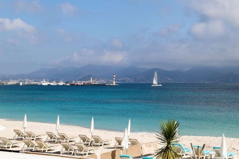 Sandy beach in Cannes with sun loungers and a distant lighthouse