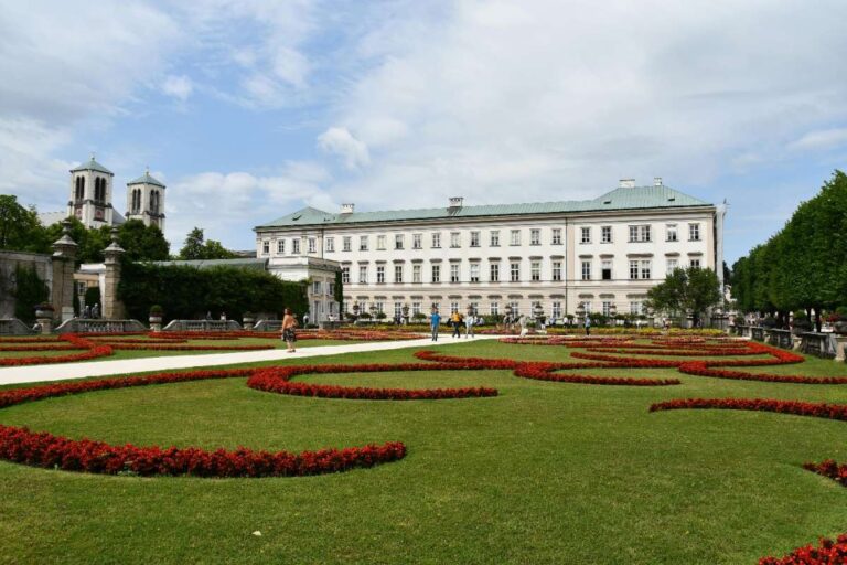 Mirabell Gardens with red flower designs and a white castle in the background