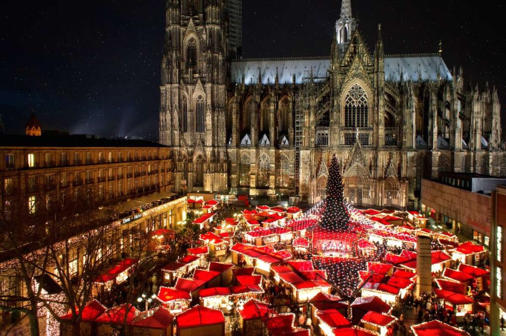 Christmas market with red stalls in front of Cologne cathedral at night