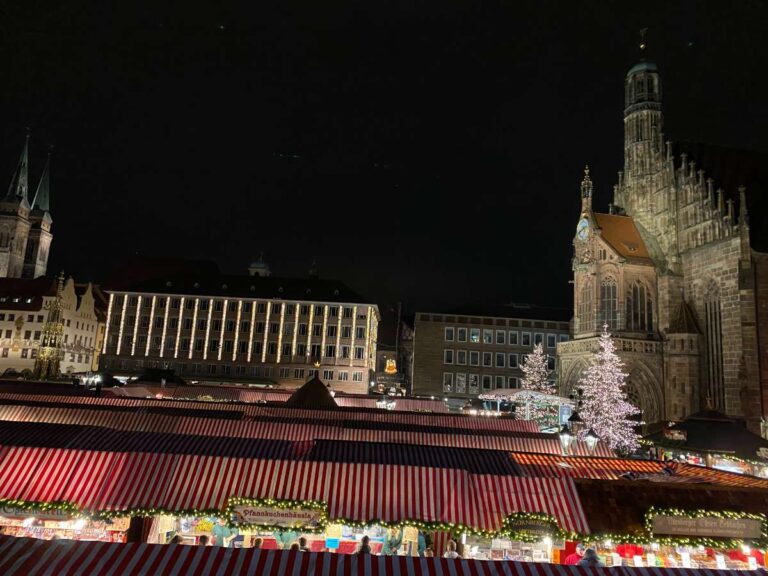 Christmas market in a historic square with lit-up stalls at night in front of Nuremberg cathedral