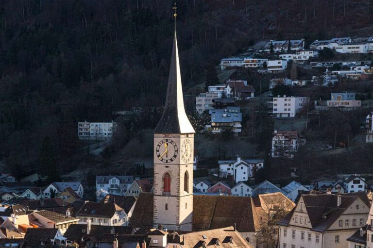 A clock tower in Chur with a background of wooded hills and houses