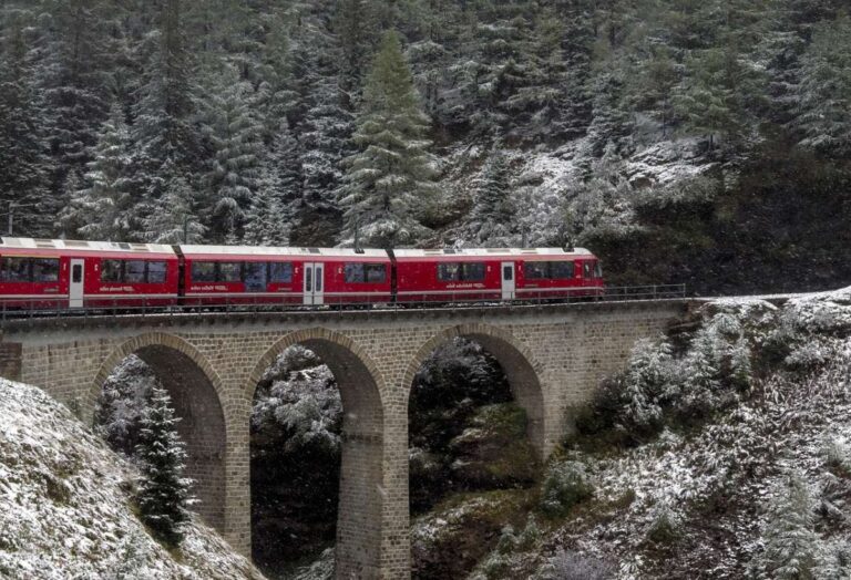 A red train crossing a stone bridge in a snowy forest landscape