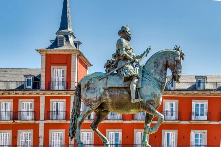 Bronze equestrian statue in front of red facade at Madrid's Plaza Mayor