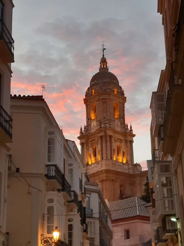 Illuminated tower of Malaga Cathedral against a dramatic sunset sky