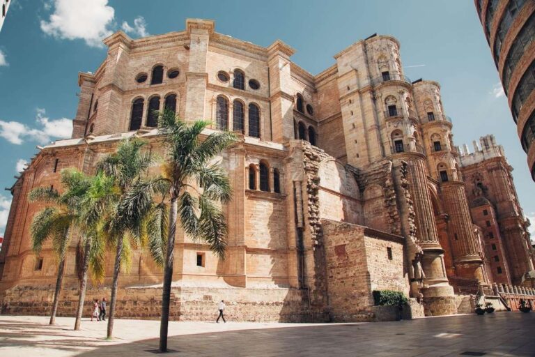 Majestic stone building in Malaga with palm trees lining the street