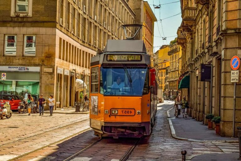 Orange tram moving through a bustling Milan street, lined with historic buildings