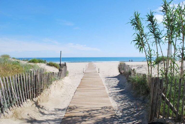 Sandy beach with a wooden walkway leading to the sea under a clear blue sky