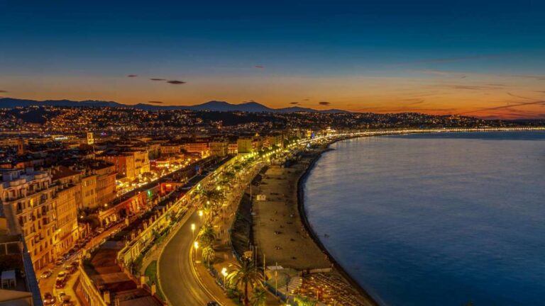 City lights illuminate the coast along Nice's beach promenade at dusk