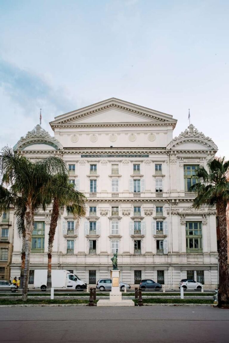 Grand, historic opera building with palm trees and cars parked in front