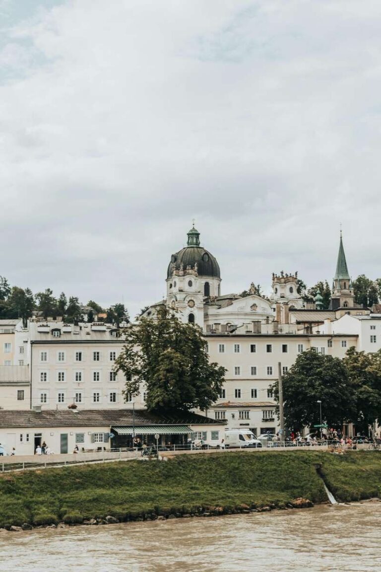 a large white building with a dome on top in front of the river in Salzburg