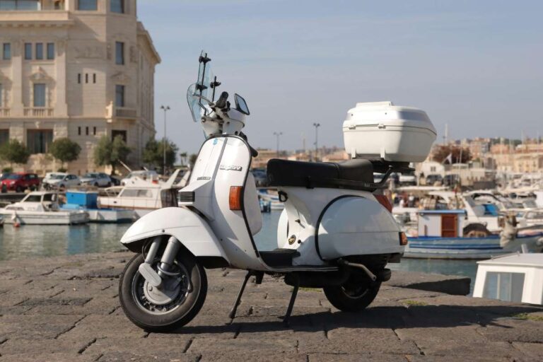 White Vespa scooter parked near a harbor with boats