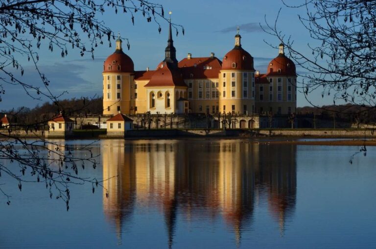 Castle reflected in a lake with a clear blue sky, framed by branches