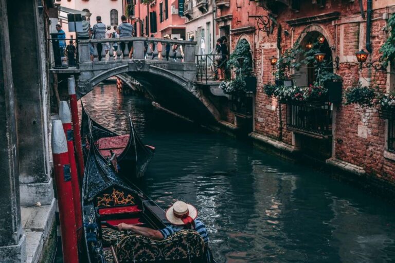 A gondolier rowing through a narrow canal in Venice under a small bridge