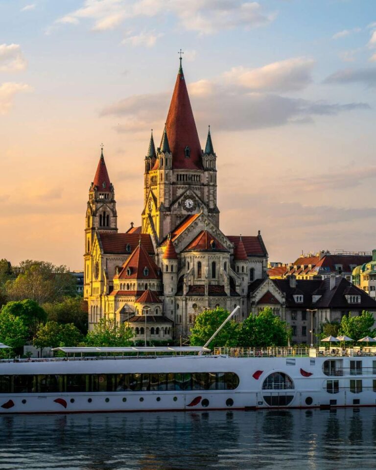 famous church of Assisi in Vienna with a clock on the top and a boat in the water in front