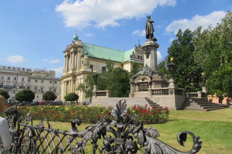 Statue surrounded by flowers and lush greenery in Warsaw under a sunny sky