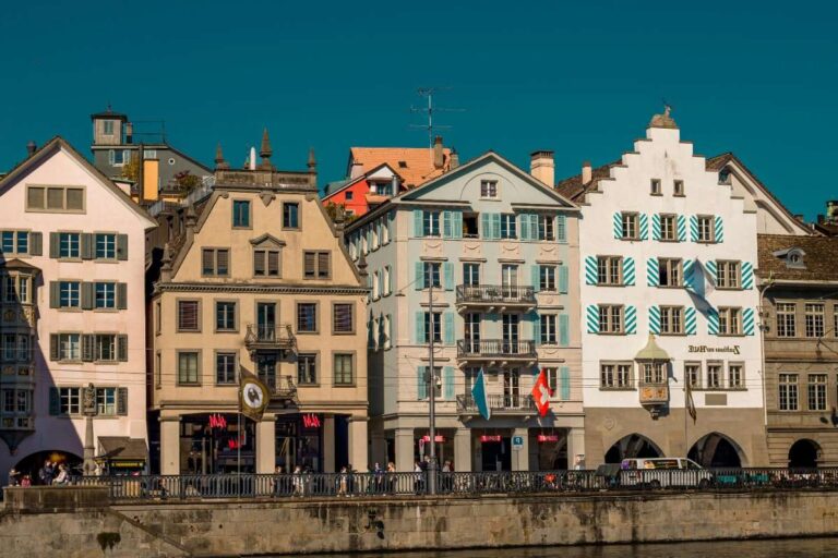 Colorful buildings along Zurich riverbank under a clear blue sky