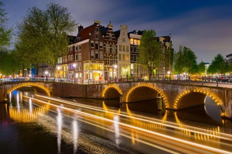 Bright lights reflecting on the canal with arched bridges and buildings in Amsterdam