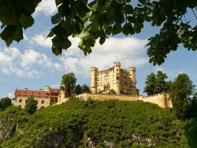 Hohenschwangau Castle perched on a hill with leafy trees and blue skies