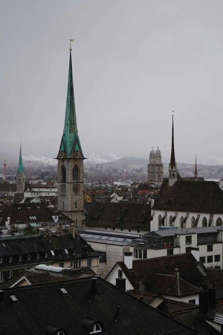 A church with a tall spire surrounded by city rooftops in Zurich