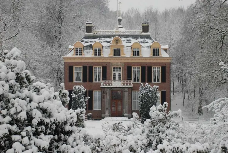 A traditional Dutch residence in Arnhem blanketed with snow and surrounded by trees