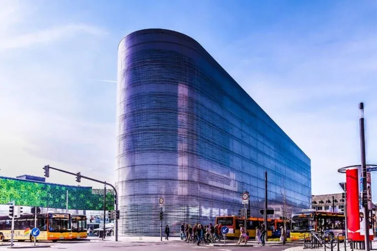 Sleek modern glass building at a busy intersection with buses and people